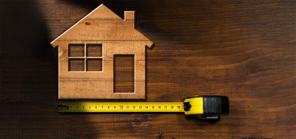 Wooden model house on a wooden table with a tape measure