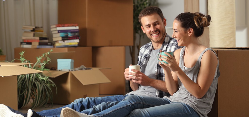 Happy couple moving into first home resting and talking the floor drinking coffee