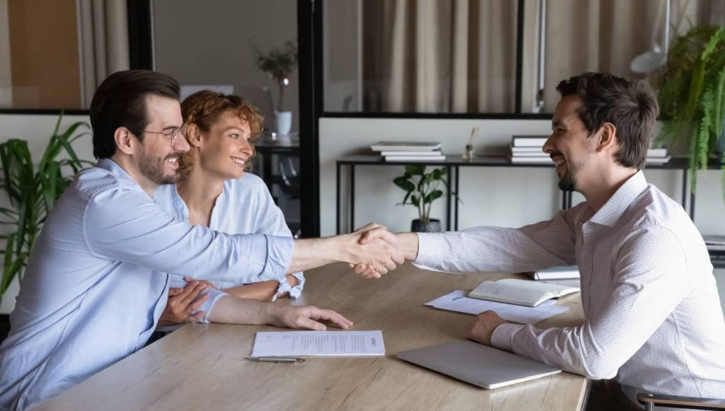 landlord or property manager meeting and shaking hands with happy couple of renters